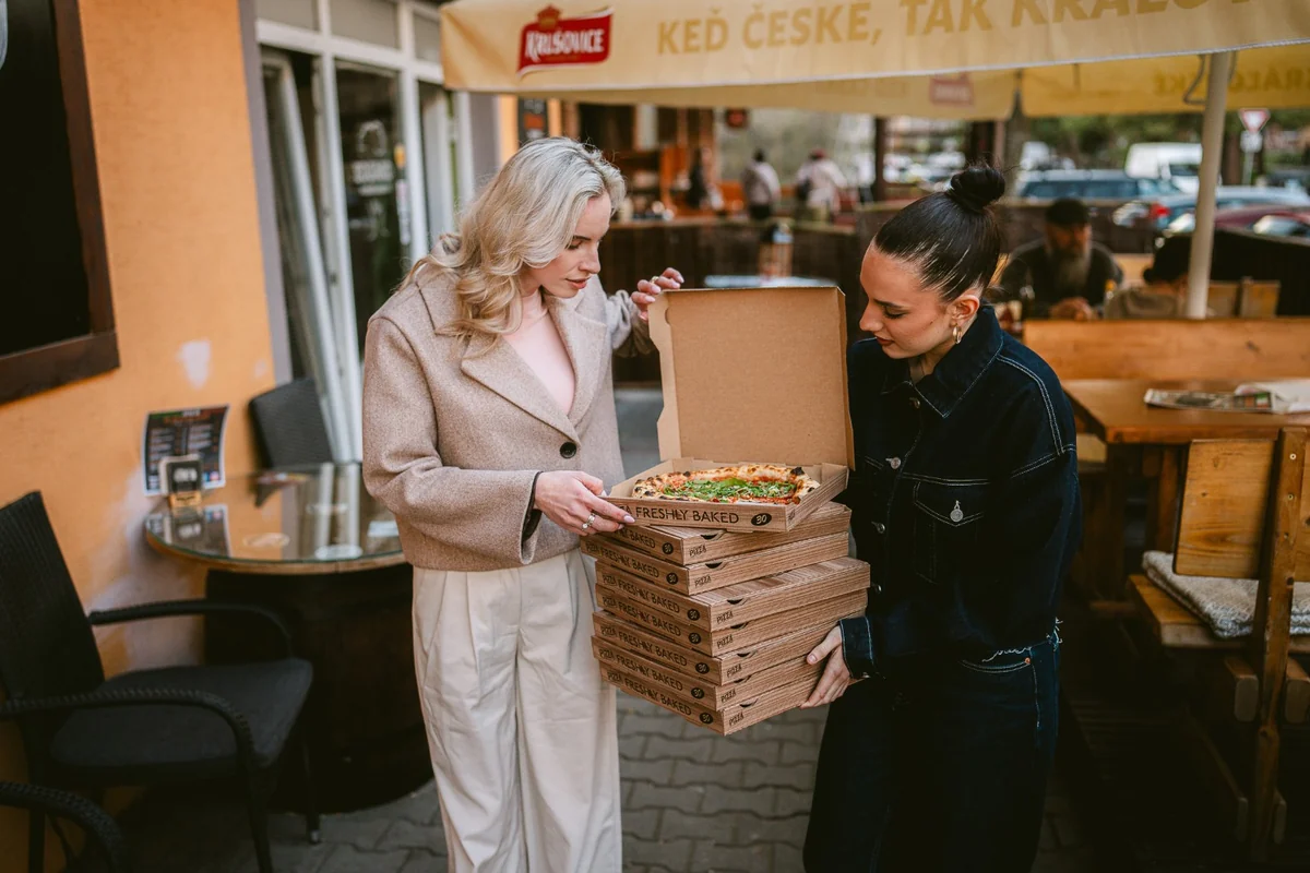Dve hostky s krabicami pizze pred podnikom